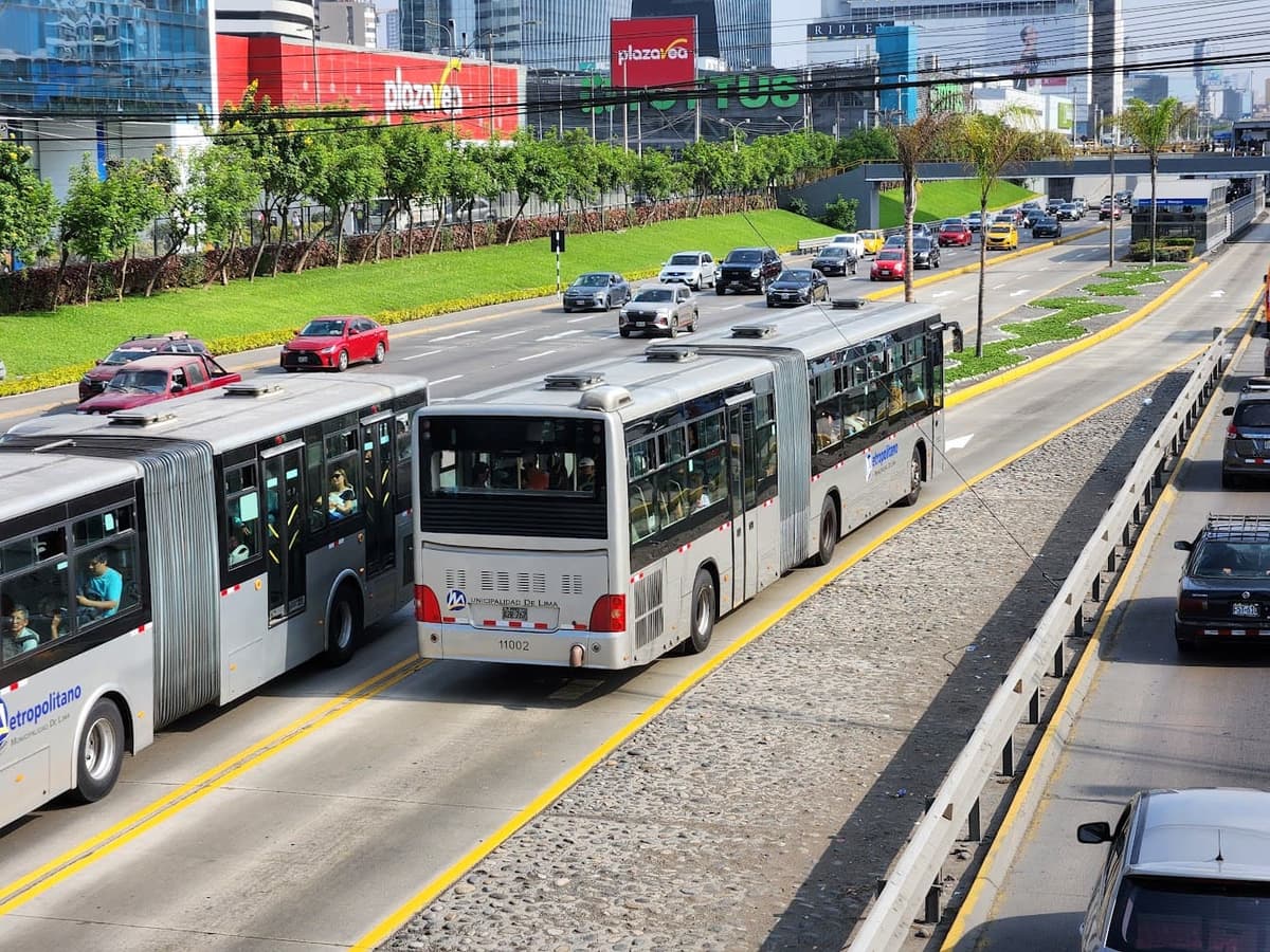 Dos buses articulados del Metropolitano en el carril exclusivo, vistos desde un puente peatonal